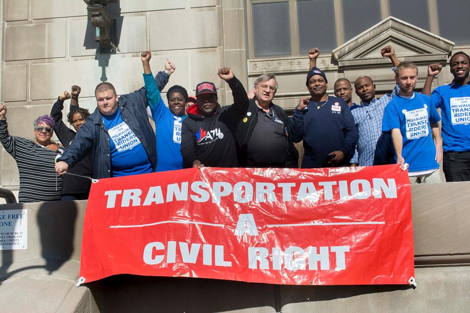 Image description: Transit riders and workers in Milwaukee unfurl a banner declaring transportation a civil right.
